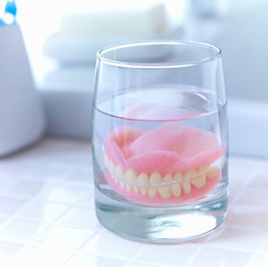 Full set of dentures in a glass of clear fluid on a tiled countertop